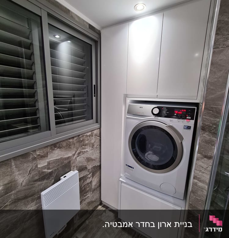 מכונת כביסה בחדר כביסה מודרני עם ארונות לבנים